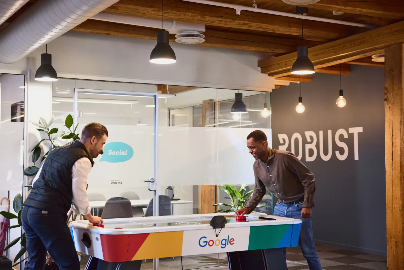 Innovative team playing table hockey in modern office with "Robust" sign.