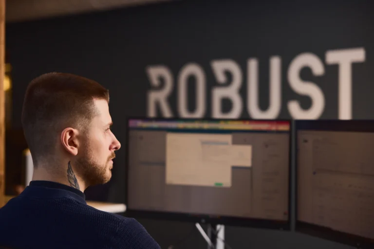 Robust logo og en person som jobber ved dataskjermer i et kontormiljø.