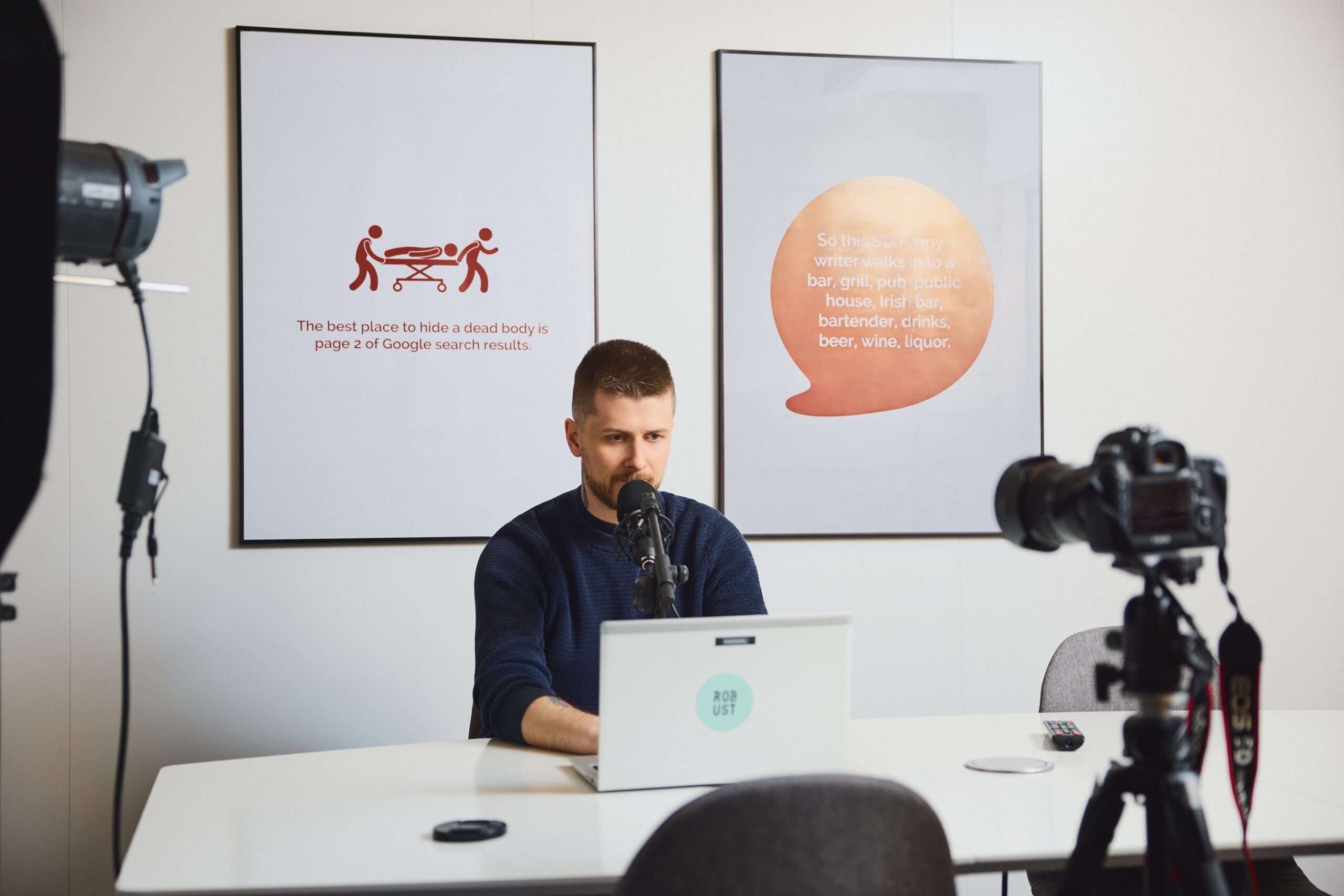 Høyt fokusert mann foran laptop i moderne kontor med kamera og plakater.