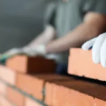 Betongarbeidere legger murstein under bygging av vegg, fokus på håndverk og konstruksjon.