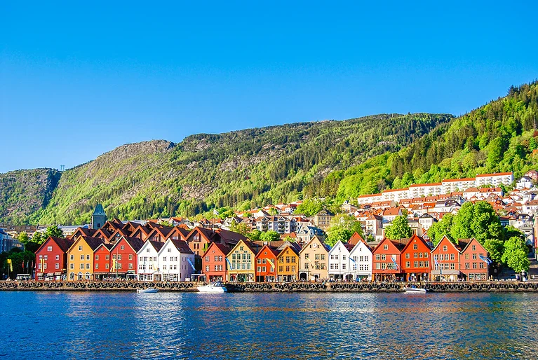 Fargerike trehus langs vannet i Bergen med fjell i bakgrunnen.