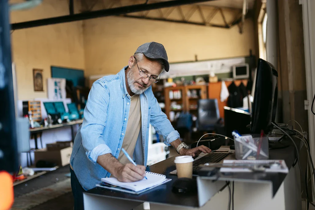Mann skriver notater ved arbeidsbord i kontorlandskap.